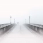 Brücke, über die ein Radfahrer fährt, der aus dem Nebel kommt