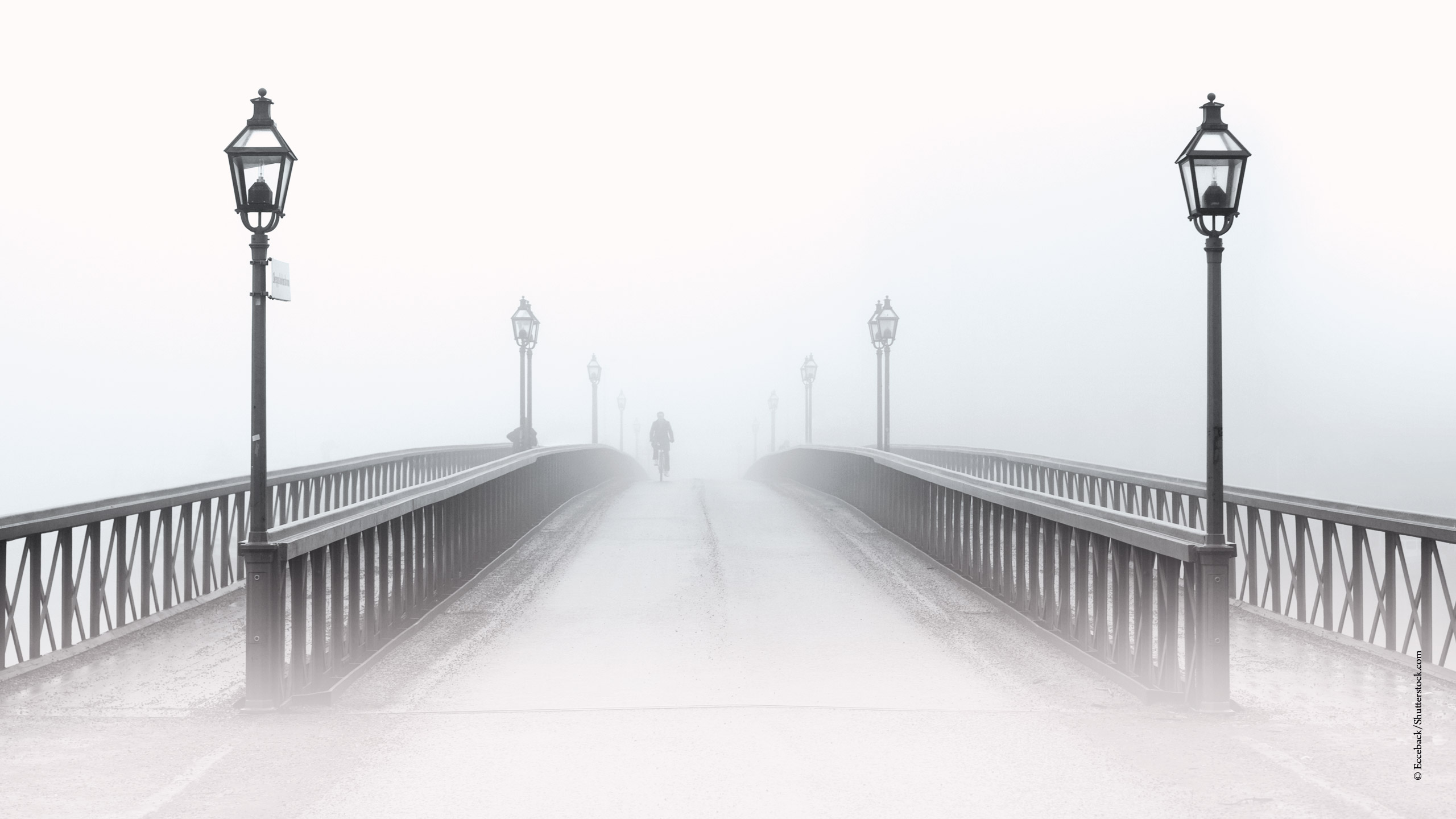 Brücke, über die ein Radfahrer fährt, der aus dem Nebel kommt